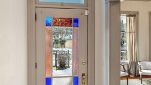 Una puerta blanca con un vitral, un ventanal pequeño arriba y suelo de madera.