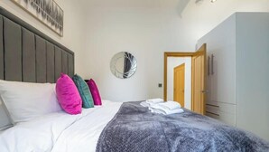 Un lit bien fait, avec des oreillers, un miroir rond et une armoire dans une chambre d’hôtel.