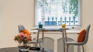 A dining area with a table, chairs, a vase of flowers, and a window with blinds.