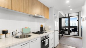Eine moderne Küche mit weißen Schränken, einer Edelstahlspüle und einem eingebauten Backofen. Durch eine Glastür ist ein Essbereich mit Tisch und Stühlen zu sehen.