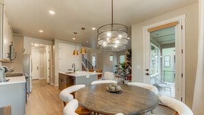 Una cocina moderna con una isla central, un comedor con una mesa redonda y sillas blancas, y una escalera que sube a un nivel superior.