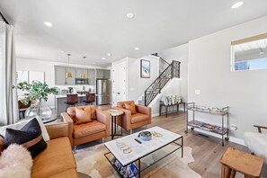 A modern living room with leather sofas, a coffee table, and a staircase leading to a kitchen area. - Deer Springs 4BR | Private Hot Tub | Deer Valley & Jordanelle Views (Hideout)