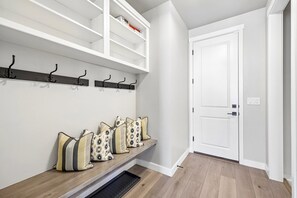 A hallway with a coat rack, a bench with cushions, and a white door. - Deer Springs 4BR | Private Hot Tub | Deer Valley & Jordanelle Views (Hideout)