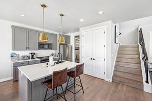 A modern kitchen with a central island, bar stools, stainless steel appliances, and pendant lighting. - Deer Springs 4BR | Private Hot Tub | Deer Valley & Jordanelle Views (Hideout)