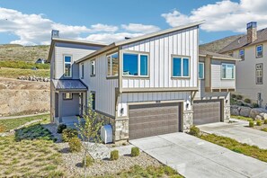 A modern two-story house with a garage, stone foundation, and a clear blue sky. - Deer Springs 4BR | Private Hot Tub | Deer Valley & Jordanelle Views (Hideout)