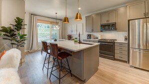 Una cocina moderna con una isla central, electrodomésticos de acero inoxidable e iluminación colgante.