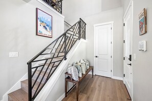 Un escalier avec une rampe en métal, un banc avec des coussins, une porte et un thermostat fixé au mur.
