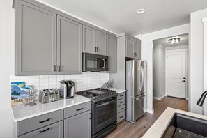 Une cuisine moderne avec des meubles gris, un réfrigérateur en acier inoxydable, un four à micro-ondes, une cuisinière et une machine à café.