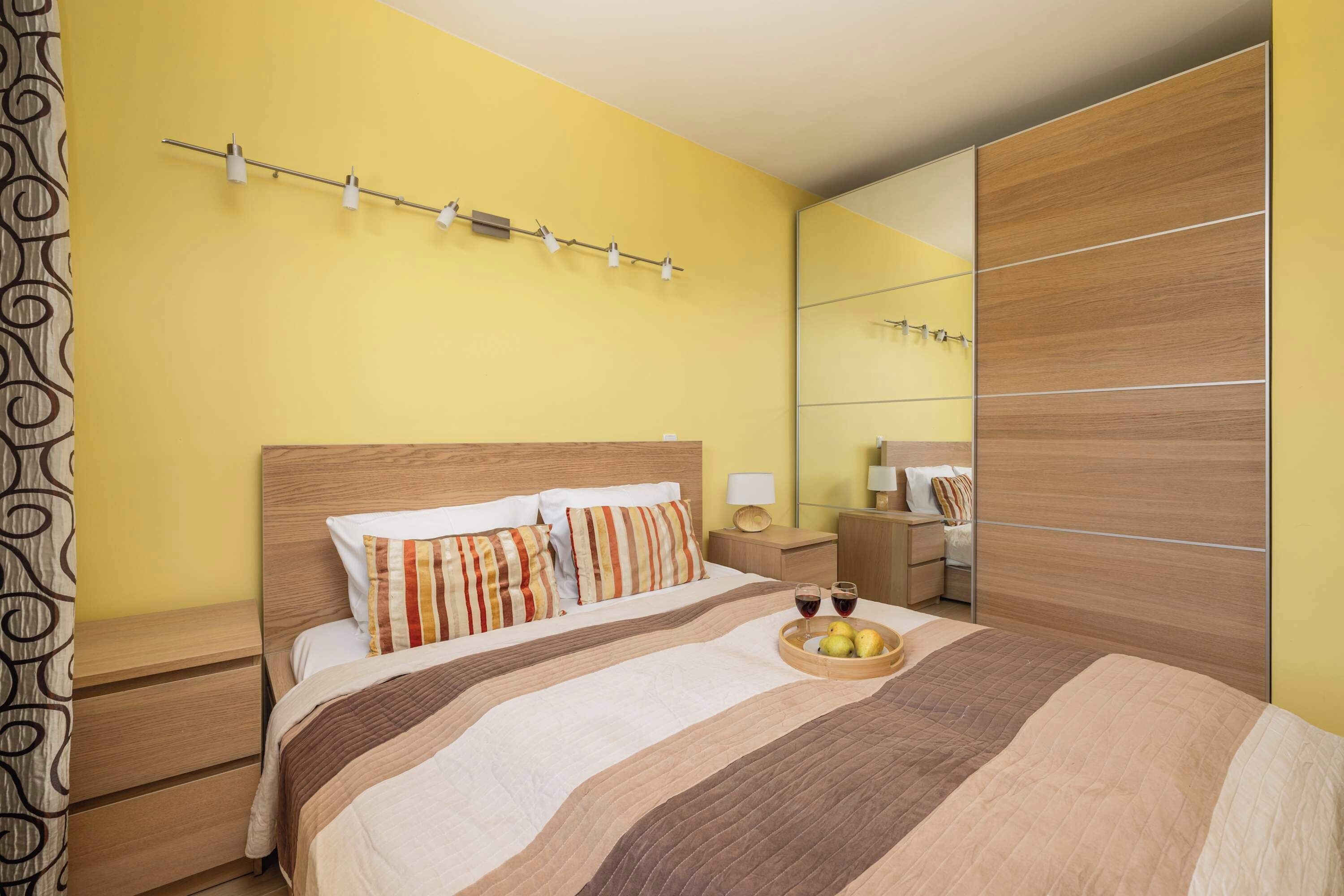 Een slaapkamer met een bed, nachtkastjes, een spiegel en een wandlamp.