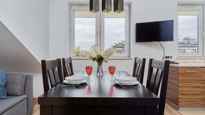A dining area with a dark wooden table, six chairs, two red glasses, a vase with white flowers, and a television on the wall. - Cozy Studio in Quiet Neighborhood | Balcony, Parking (Wrocław)