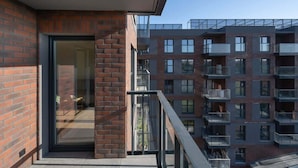 A modern apartment building with a glass door entrance, balconies, and a brick facade.