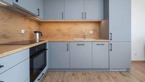A modern kitchen with grey cabinets, a wooden countertop, a built-in oven, and a sink.