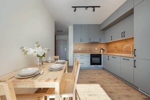 Une cuisine moderne avec des meubles gris, un plan de travail en bois et un coin repas comprenant une table et des chaises en bois.