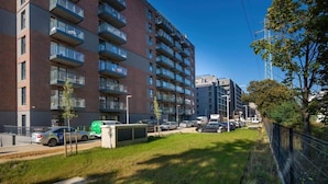 A multi-story residential building with balconies, a parking area, and a small green space.