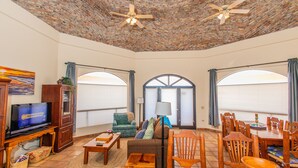 A spacious living room with a brick ceiling, a television, a sofa, a dining table with chairs, and large windows. - Casa Serena 3 Bed 2 Bath By FMI Rentals (Puerto Peñasco)