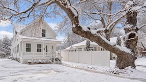 A white two-story house with a porch and a large tree in the foreground.