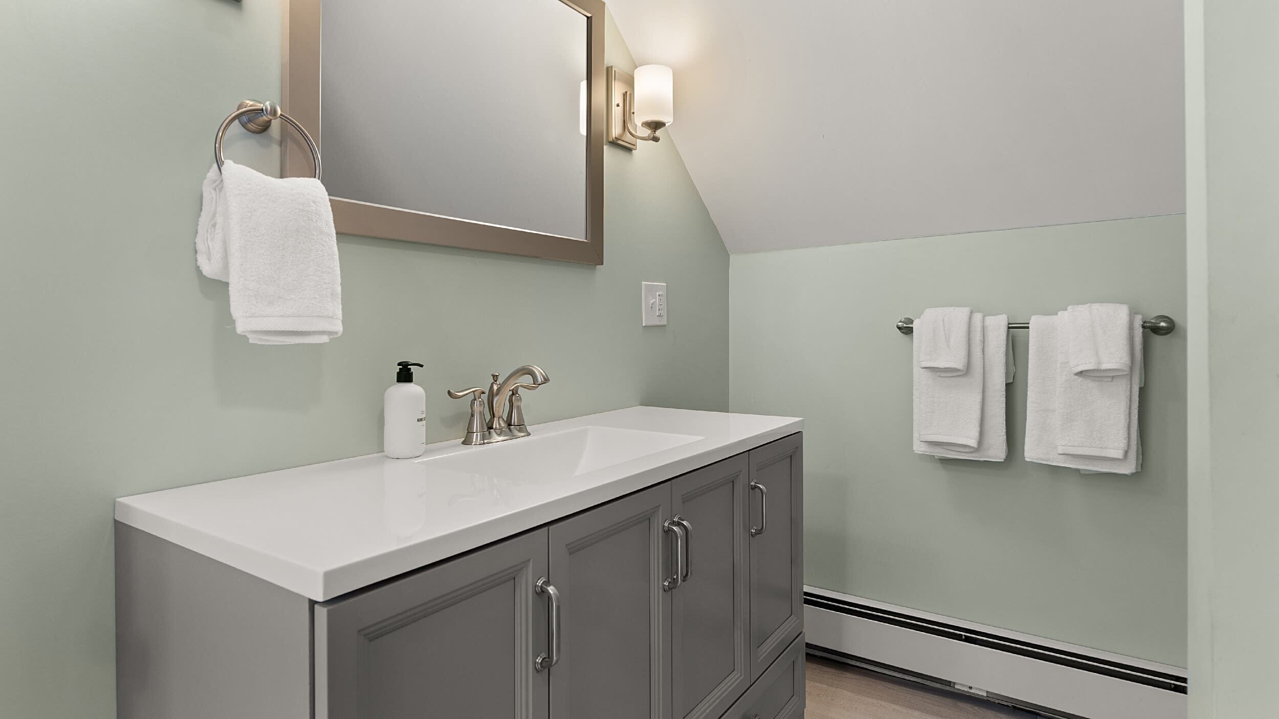 A bathroom with a white sink, a mirror, and two towel racks.