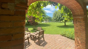 A brick archway leading to a patio with a table and chairs, surrounded by greenery and a clear sky. - Farmhouse with Farm in the hills of Barga: Casa Chioi (barga)
