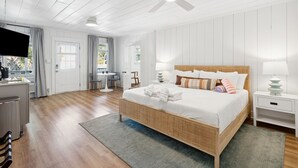 Une chambre spacieuse avec un grand lit, un ventilateur de plafond, une télévision et un coin cuisine.