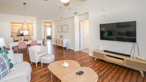 A modern living room with a flat-screen TV, a ceiling fan, and a dining area with a kitchen in the background. - Seaside at Anastasia E305 - Stunning beach rental with great location (St Augustine)