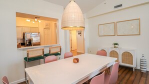 A dining area with a white table, pink chairs, and a hanging light fixture. - Seaside at Anastasia E305 - Stunning beach rental with great location (St Augustine)