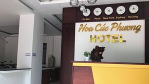 A hotel reception desk with a clock above displaying times for Ha Noi, Paris, New York, Sydney, and Beijing. - Hoa Cuc Phuong Hotel Di An - Binh Duong (Ho Chi Minh City)