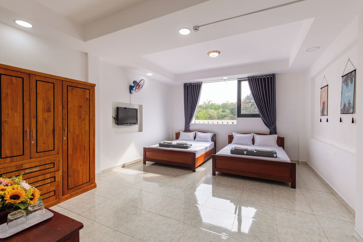 A hotel room with two beds, a wooden wardrobe, a TV, and a window with curtains.