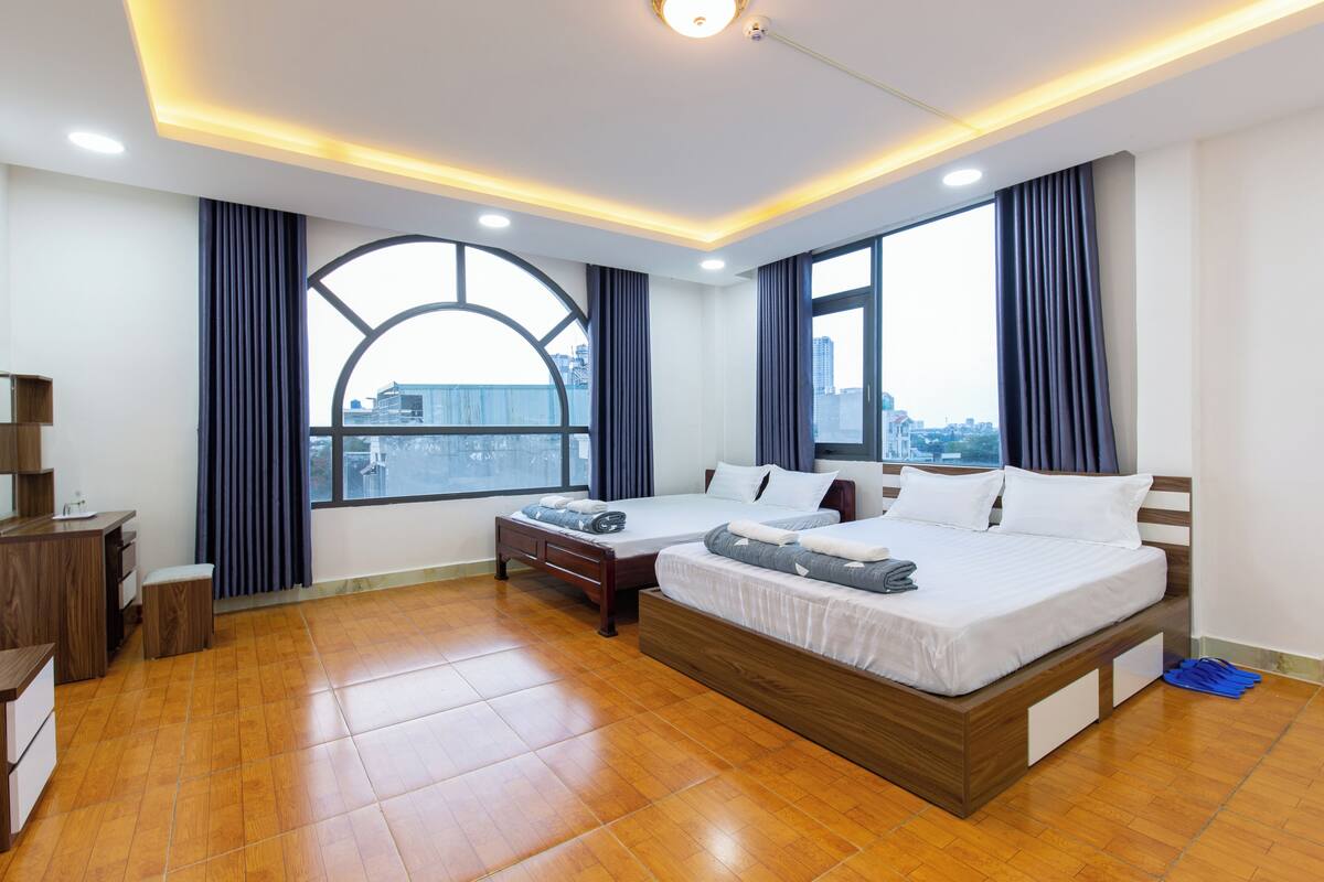 A modern hotel room with a large bed, a desk, and a view of the city through a large window.