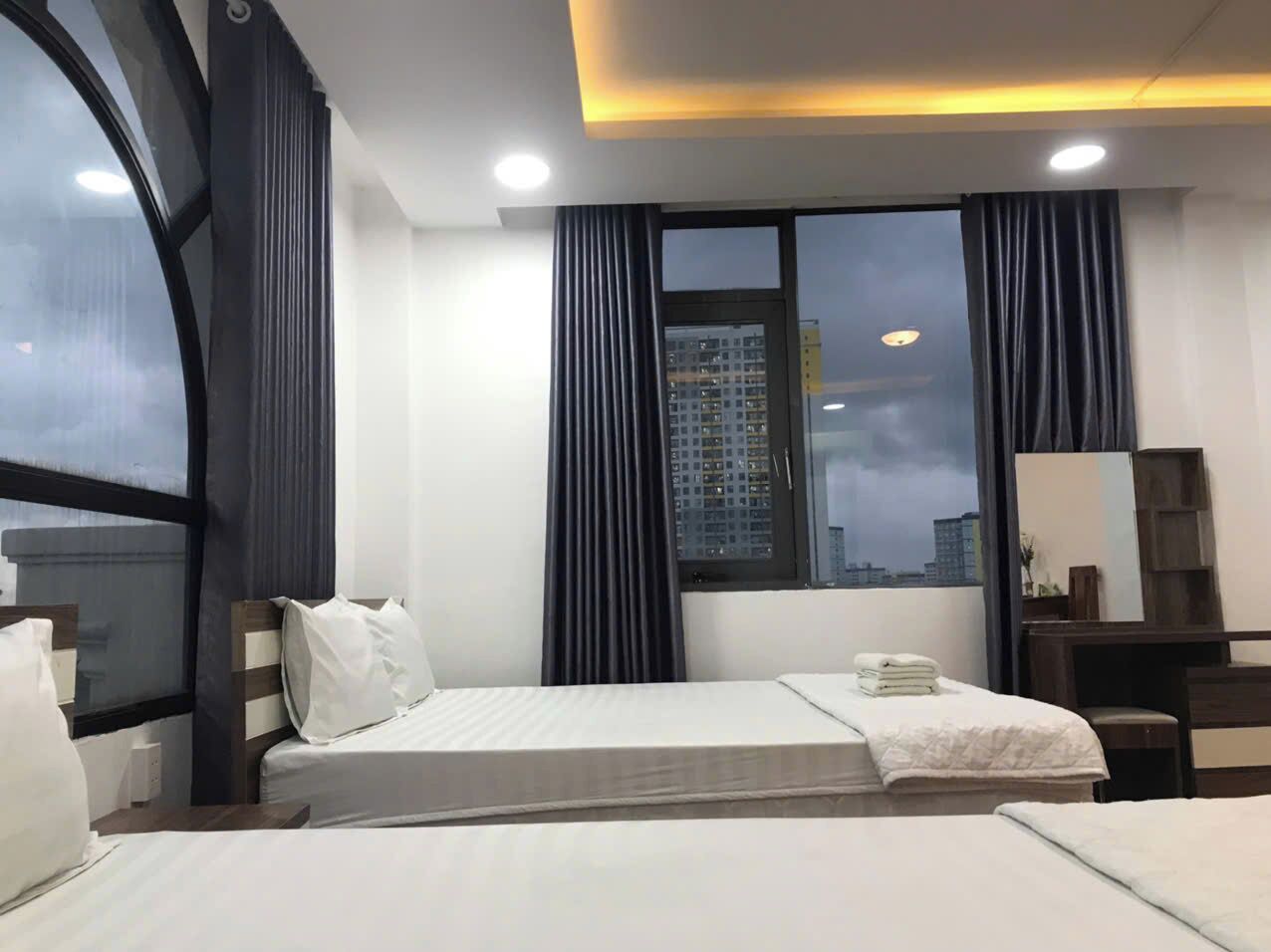 A hotel room with two beds, a large window with curtains, a desk with a chair, and a mirror.