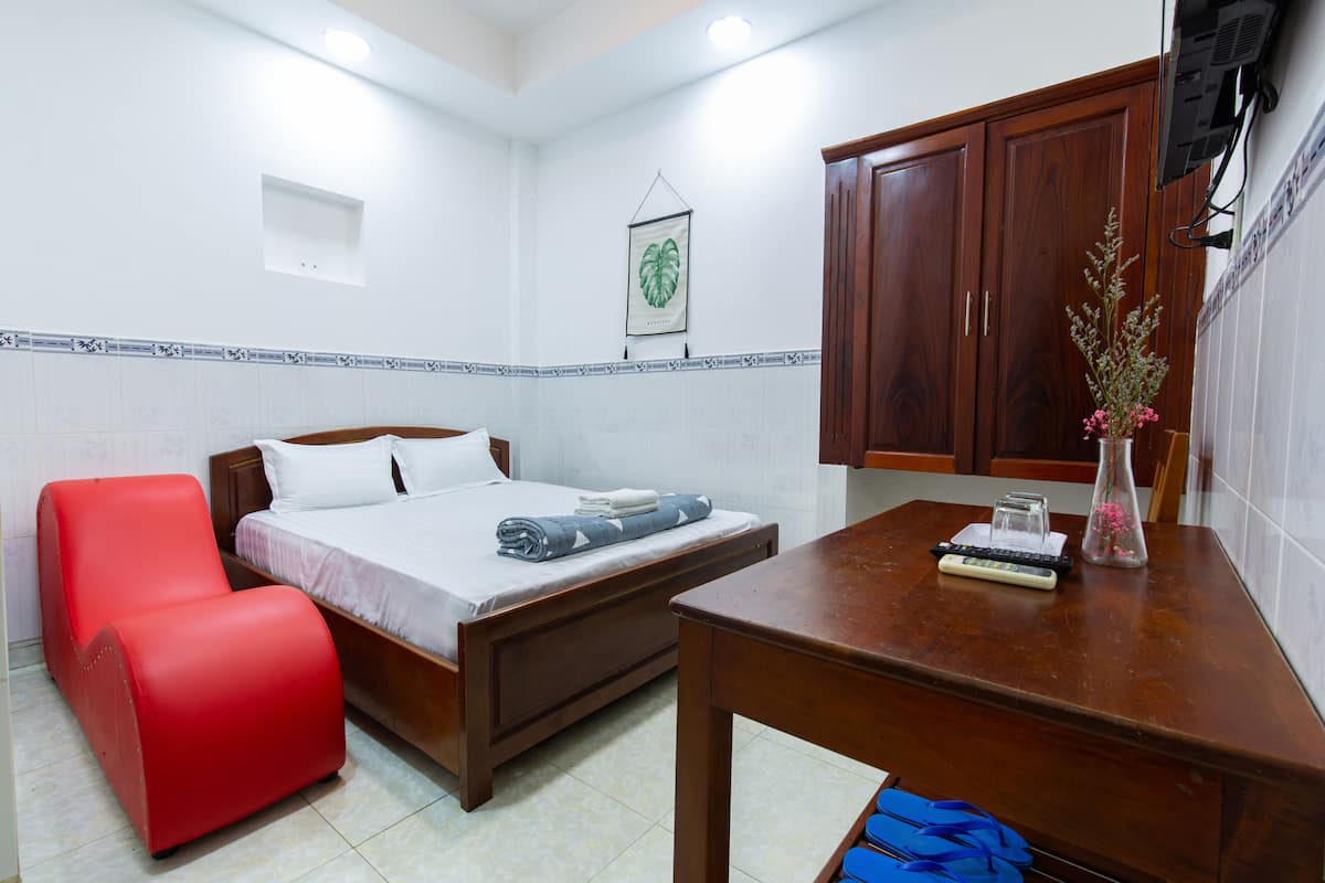 A bedroom with a bed, a red chair, a wooden table, and a TV mounted on the wall.