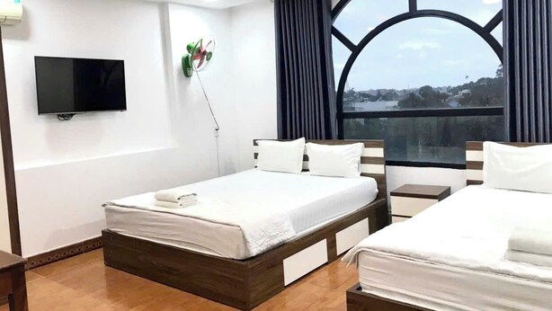 A hotel room with a large bed, a TV mounted on the wall, and a window with a view of the city. - Hoa Cuc Phuong Hotel Di An - Binh Duong (Ho Chi Minh City)