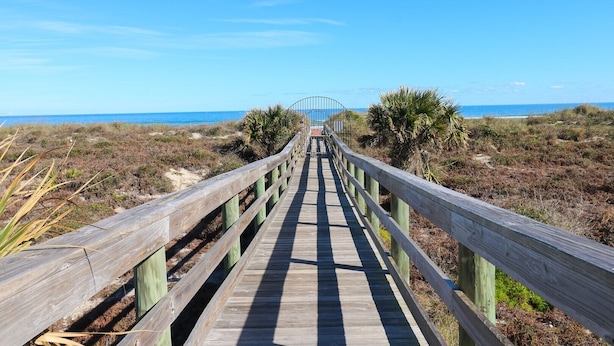 Un paseo marítimo de madera que conduce a una playa, con una reja metálica al final.