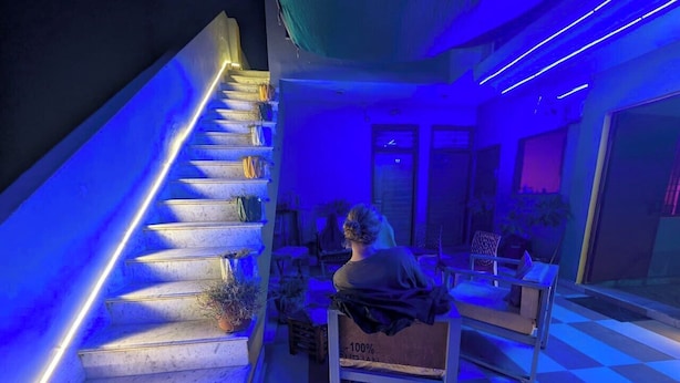 A staircase with blue lighting, a checkered floor, and a person sitting on a bench. - Taj Street Hostel (Agra)
