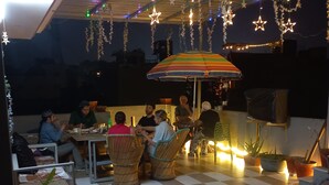 An outdoor dining area with checkered flooring, wicker furniture, and potted plants. - Taj Street Hostel (Agra)