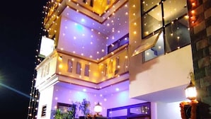 A multi-story building with balconies, string lights, and a gated entrance. - Taj Street Hostel (Agra)