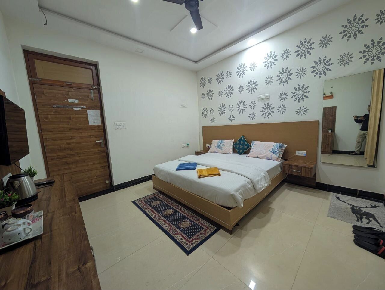 A bedroom with a bed, a wooden door, a mirror, and a patterned rug.