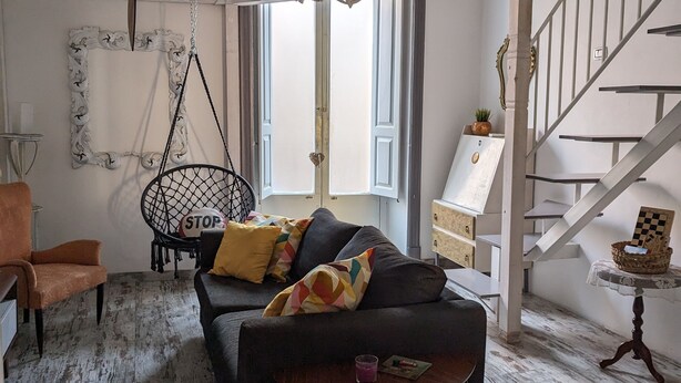 A living room with a black sofa, a wooden floor, a hanging clock, and a staircase. - Lovely space with terrace in the old town! (Catania)