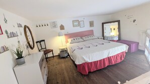 A bedroom with a wooden floor, a bed with a pink headboard, a bedside table with a lamp, a chair, and a dresser. - Lovely space with terrace in the old town! (Catania)