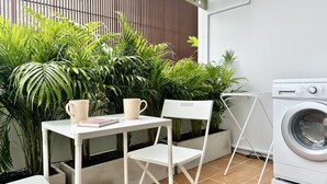 A small, clean room with a washing machine, a table with two chairs, and a variety of green plants. - The Tangerine Guesthouse (Bangkok)