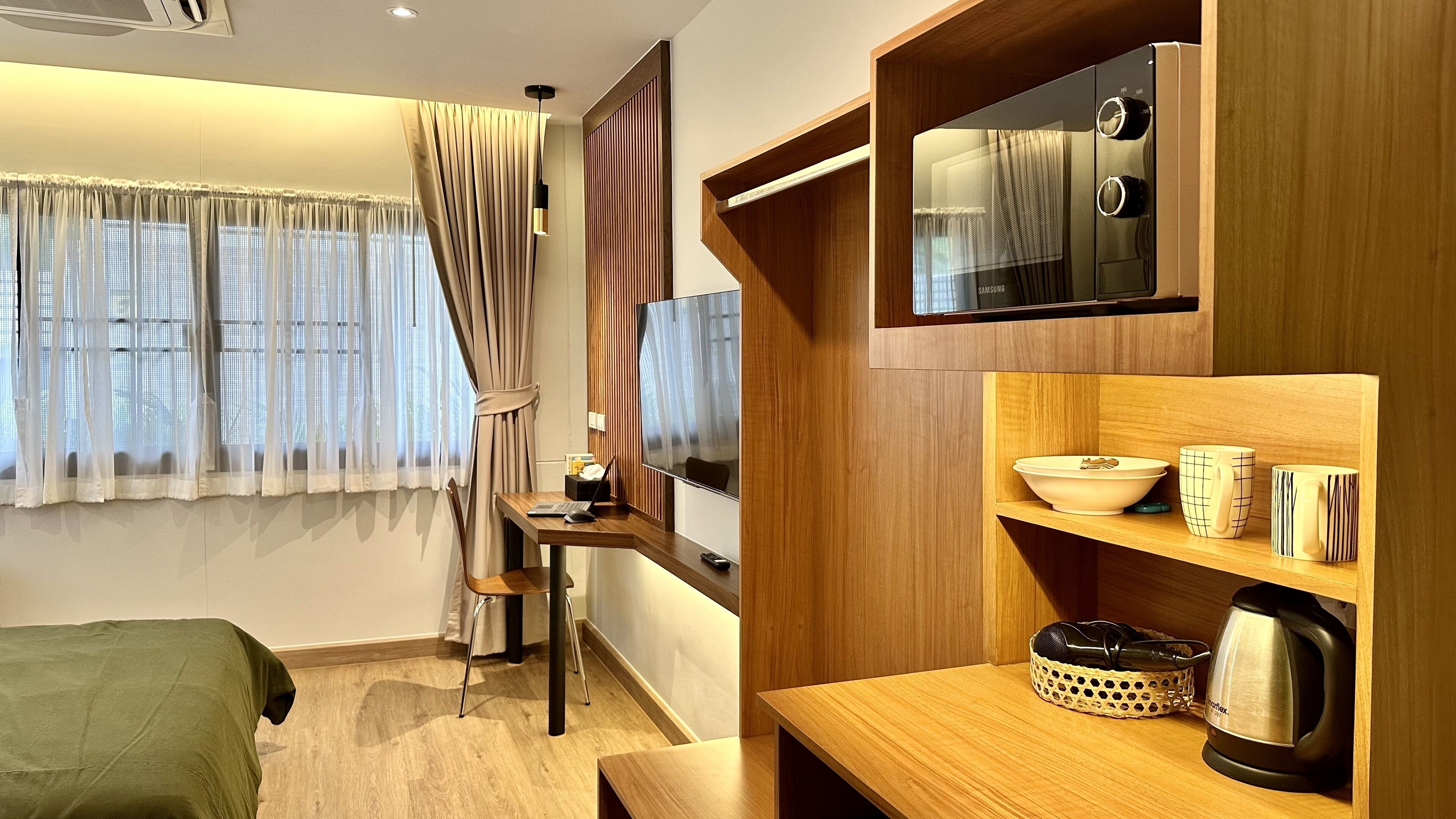 A modern hotel room with a wooden desk, a laptop, a bowl, and a kettle.