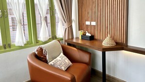 A modern room with a leather chair, a wooden side table, and a green-framed window with white curtains. - The Tangerine Guesthouse (Bangkok)