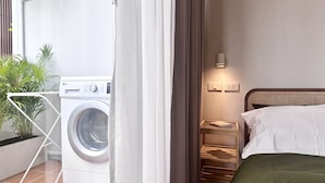 A hotel room with a washing machine, a bedside table with a book, and a green bedspread. - The Tangerine Guesthouse (Bangkok)