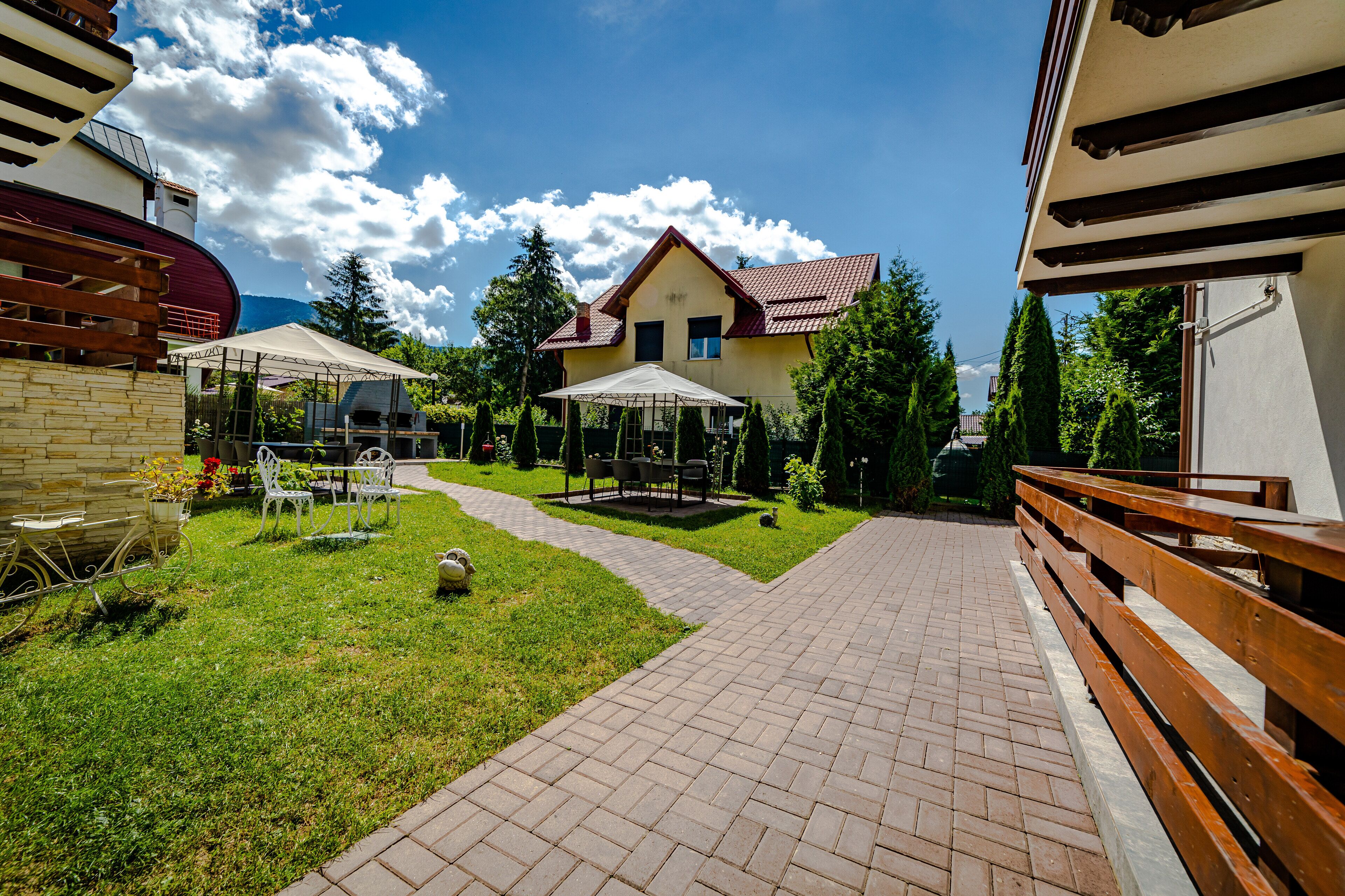 A courtyard with a paved walkway, outdoor seating, and a building with a red roof.