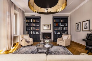 Una sala de estar con dos sillones, una mesita de centro, una chimenea y dos estanterías llenas de libros y objetos decorativos.