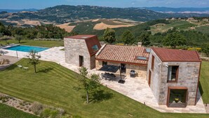 Uma casa moderna com piscina, fachada de pedra e vista para colinas ondulantes.