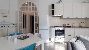 Cozinha compacta com armários brancos, fogão, forno e pia. Há uma área de jantar com mesa e cadeiras.