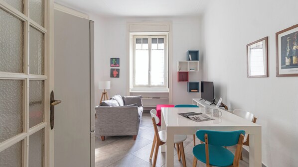 A modern living room with a sofa, a dining table with chairs, a TV, and a bookshelf.