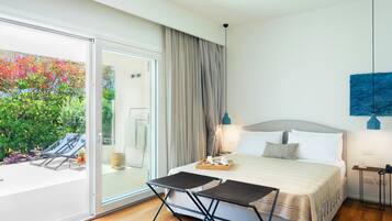 A modern hotel room with a large bed, a dining table, and a view of a garden with colorful plants.