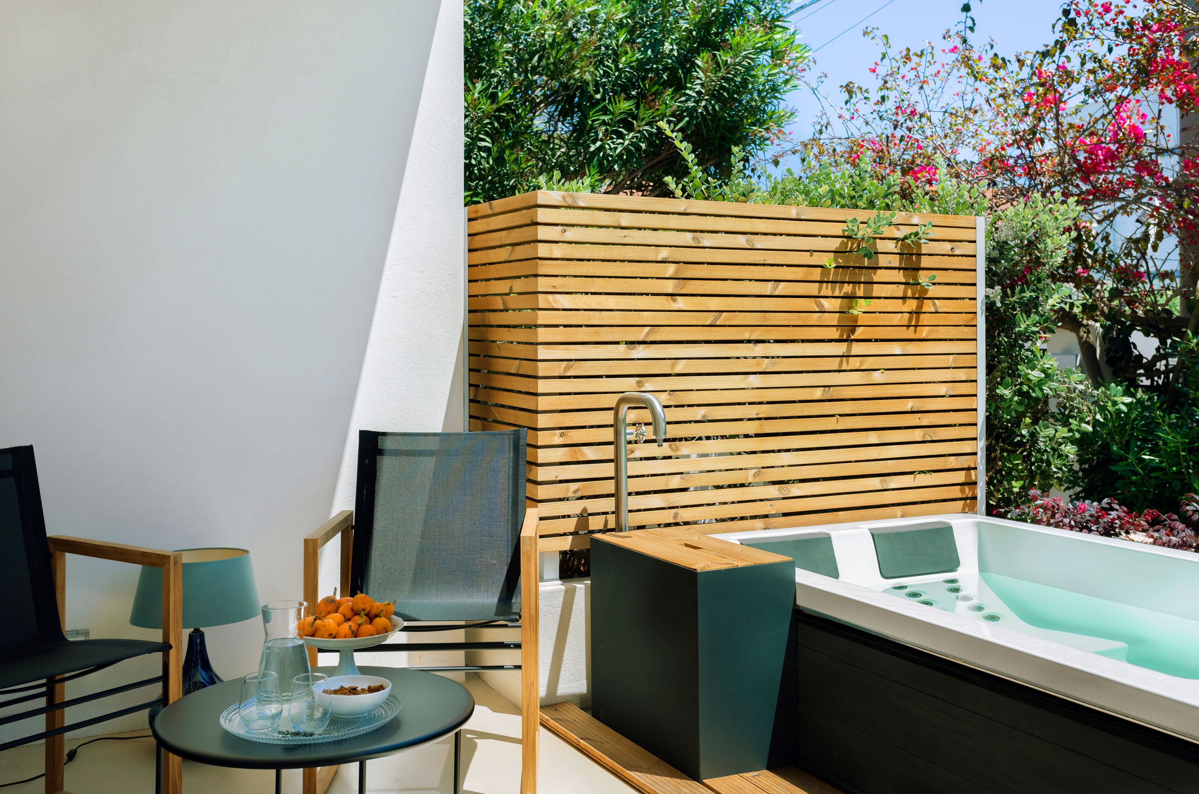 A modern outdoor area with a wooden deck, a seating area with chairs and a table, a small fountain, and a hot tub.
