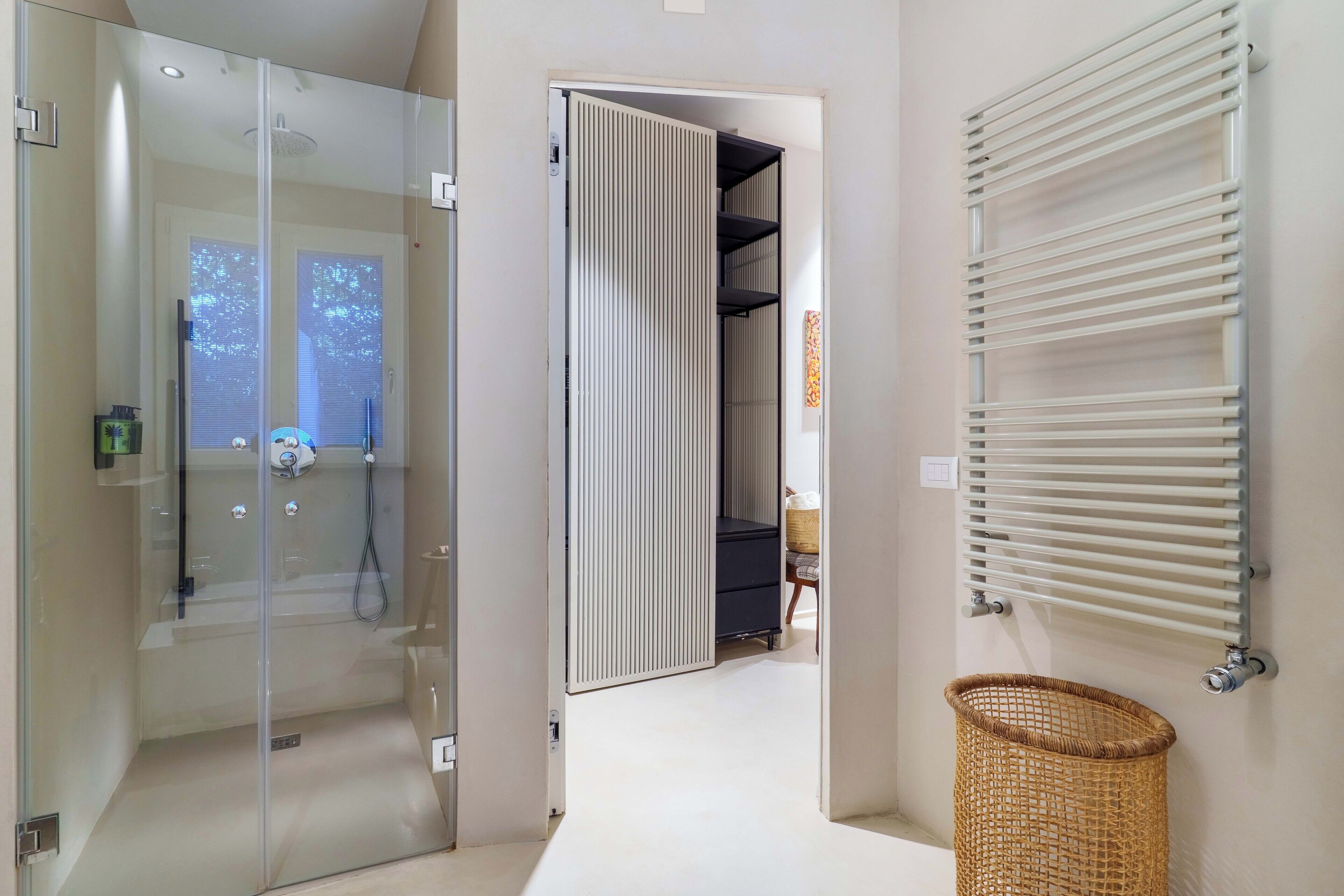 A modern bathroom with a glass shower enclosure, a white radiator, and a wicker basket.